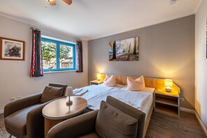 Een hotelkamer met een bed, twee nachtkastjes, een ronde tafel en twee fauteuils.