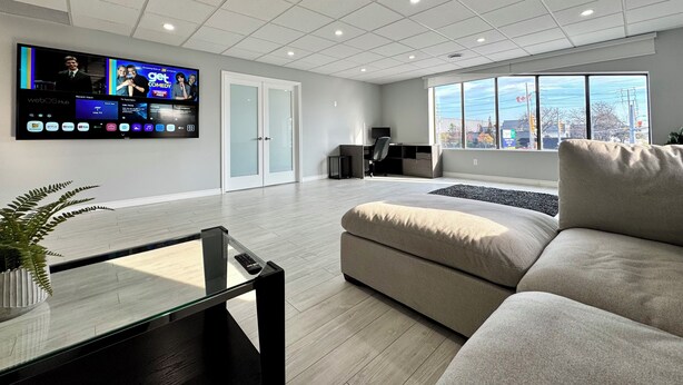 Una sala de estar moderna con un televisor de pantalla plana grande montado en la pared, un sofá cómodo, una mesa de centro de vidrio y vistas a la ciudad a través de grandes ventanales.