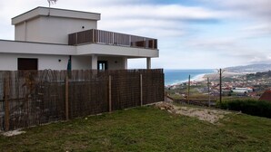A modern two-story building with a balcony, a view of the beach, and a distant town.