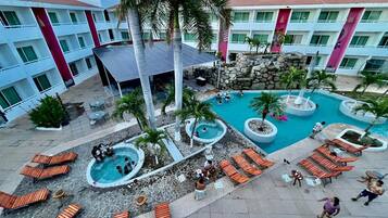 A hotel with multiple swimming pools, lounge areas, and a mountainous backdrop.