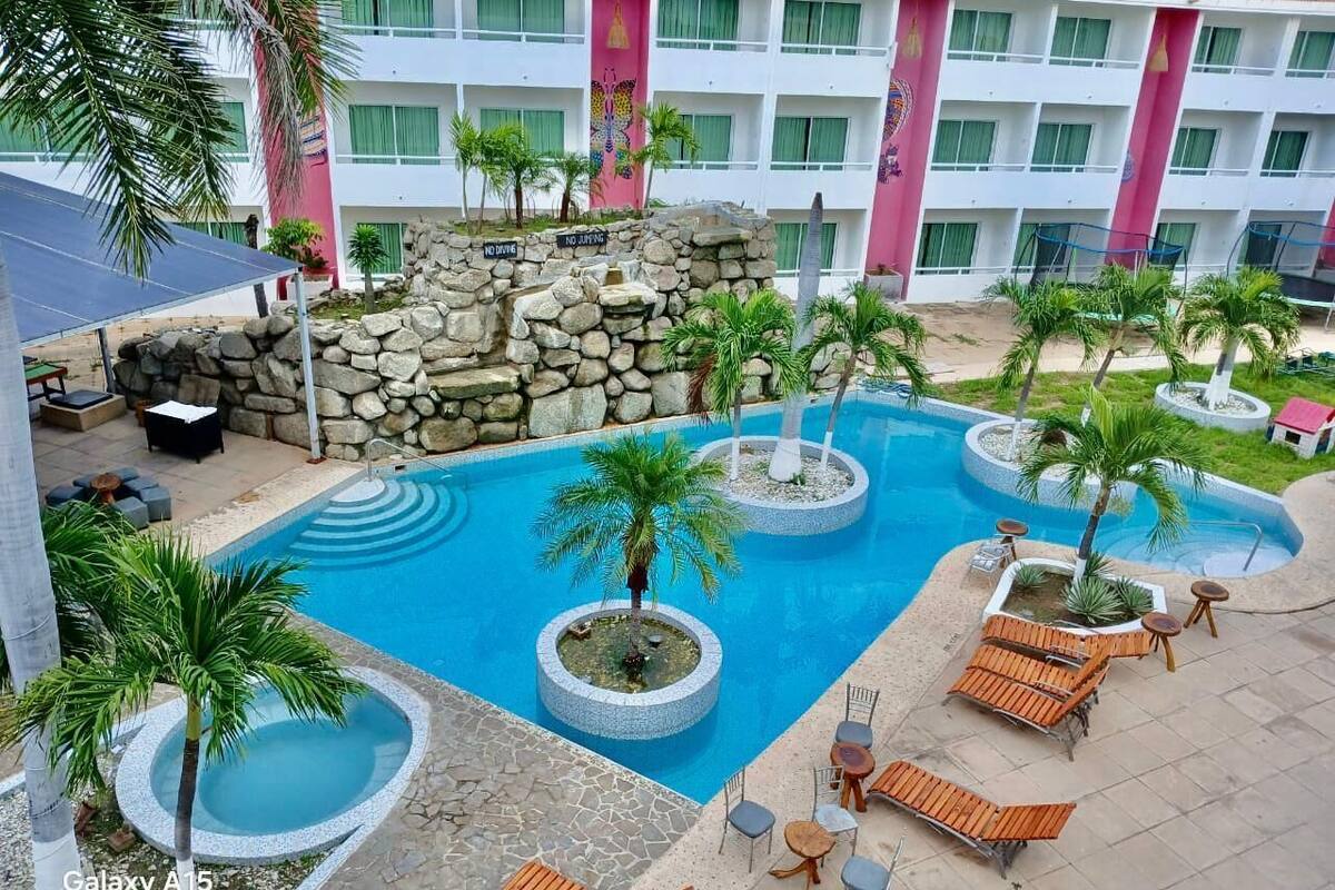 Un espace piscine d’hôtel comprenant plusieurs éléments décoratifs aquatiques de forme circulaire, des chaises longues et des palmiers.