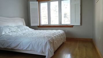 Una camera da letto con un letto, pavimento in legno, una finestra con persiane e una testiera bianca.