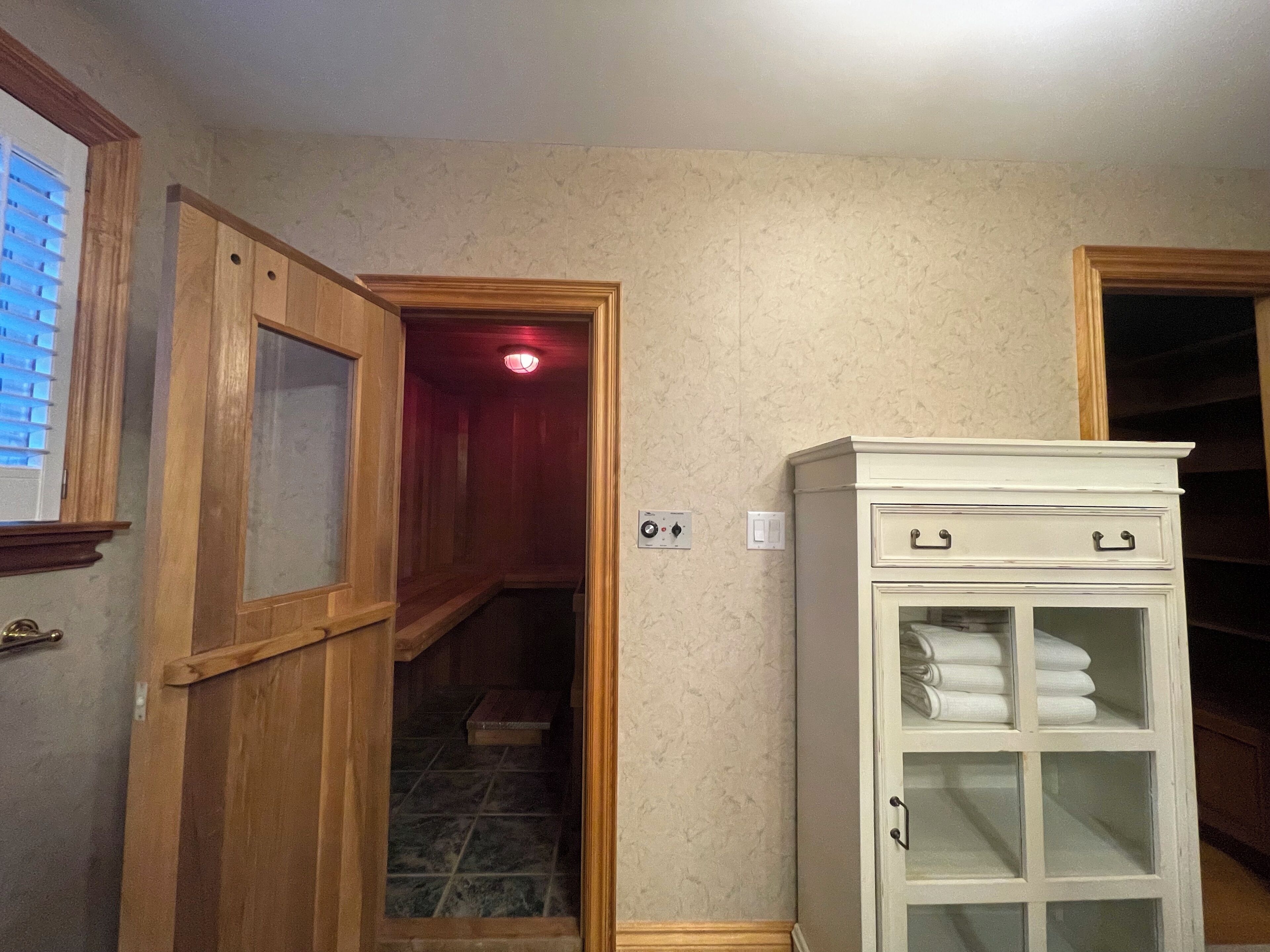 Un passadís amb una porta de fusta que dona a una escala, un armari blanc amb portes de vidre i un interruptor de llum a la paret.