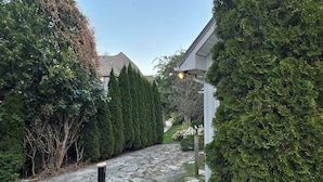A stone pathway leading to a house with a well-maintained garden and tall evergreen trees. - Lakefront Cottage w/Hot Tub, BBQ Grill, Deck, Fire Pit, Fire Place, Sauna, Dock. (Beaverton)