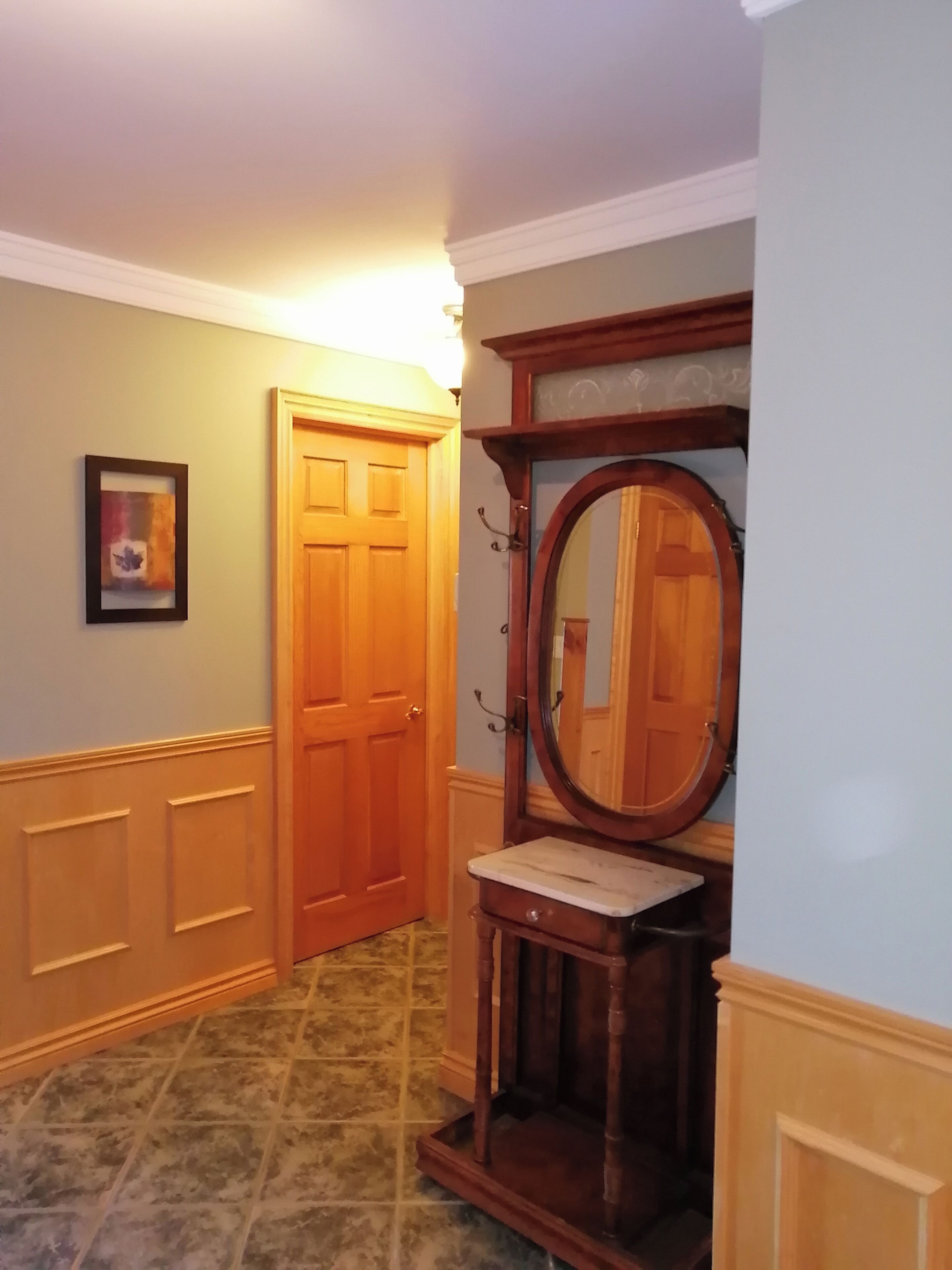 Un couloir avec une porte en bois, un tableau encadré au mur et une coiffeuse avec un miroir.