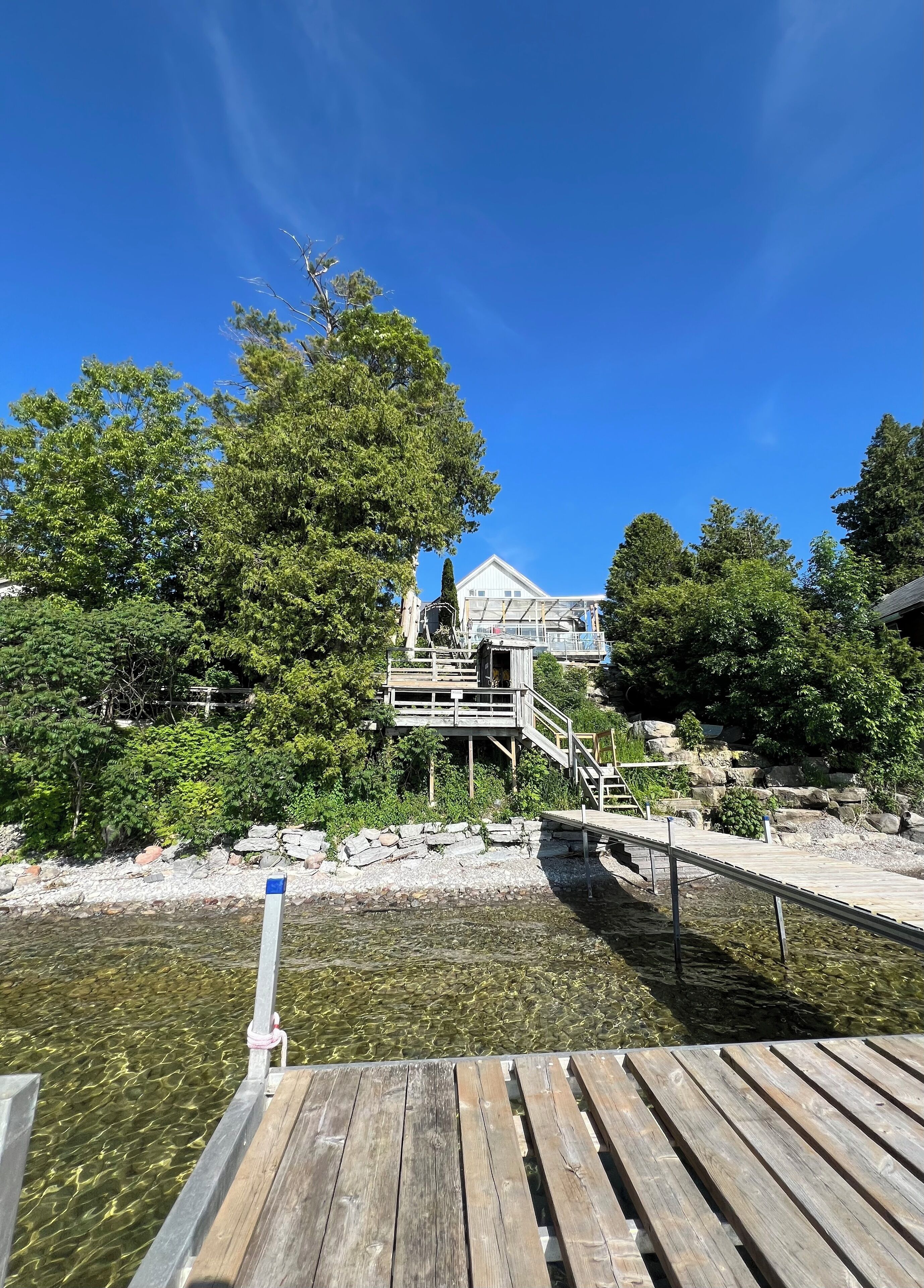 A wooden dock leading to a house with a deck and a small staircase.