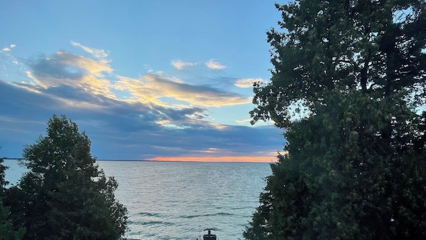 A deck with a view of the sea and sunset. - Lakefront Cottage w/Hot Tub, BBQ Grill, Deck, Fire Pit, Fire Place, Sauna, Dock. (Beaverton)