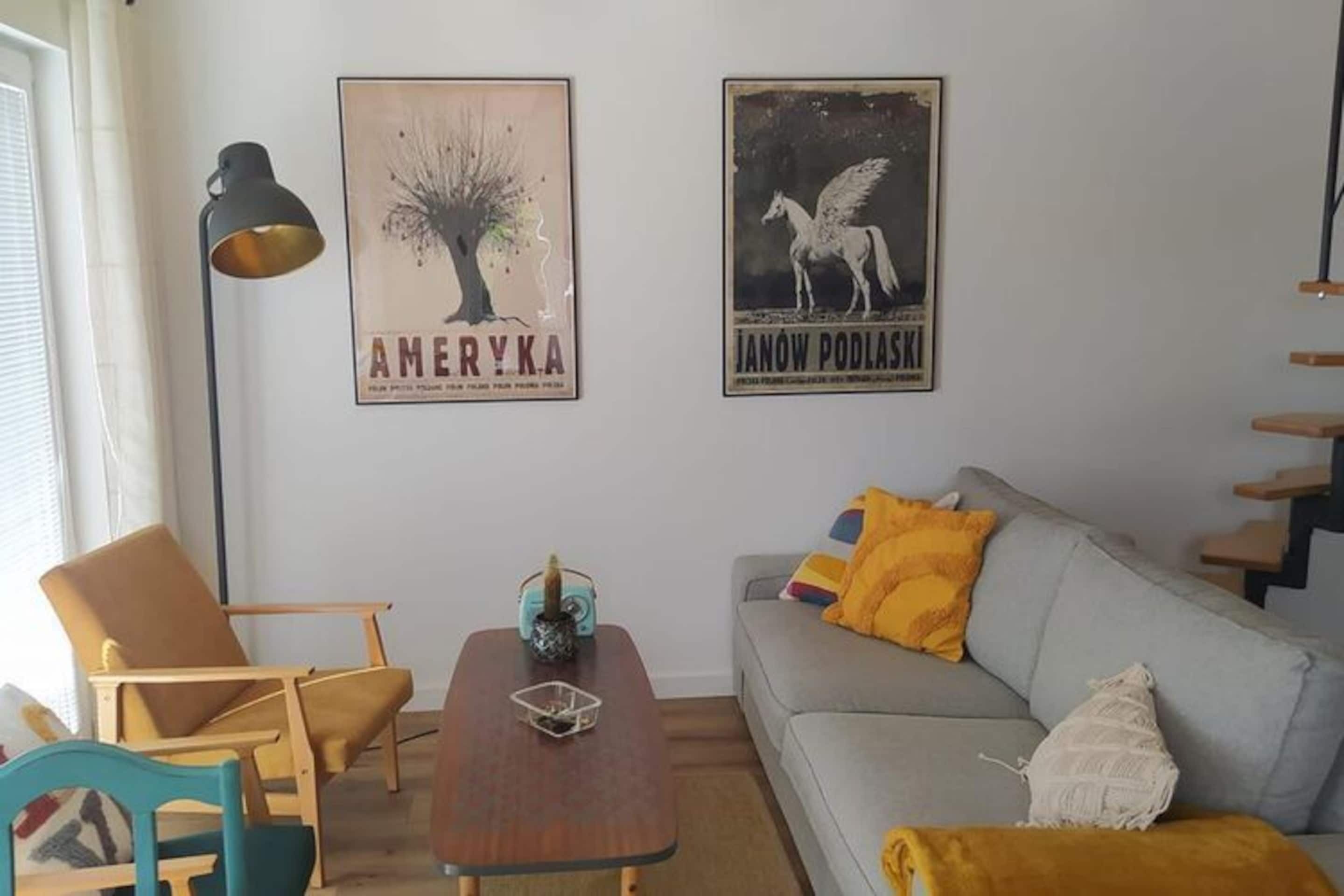 A living room with a grey sofa, yellow pillows, a wooden coffee table, and two framed posters on the wall.