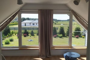 Una stanza con un'ampia finestra che si affaccia su un giardino e un edificio bianco.