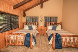 Two beds with slatted headboards, patterned bedding, and a throw blanket, set against a rustic backdrop of wooden beams.