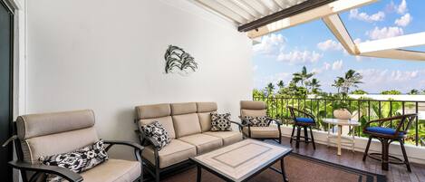 A covered outdoor seating area with a sofa, chairs, and a table, overlooking a lush garden.