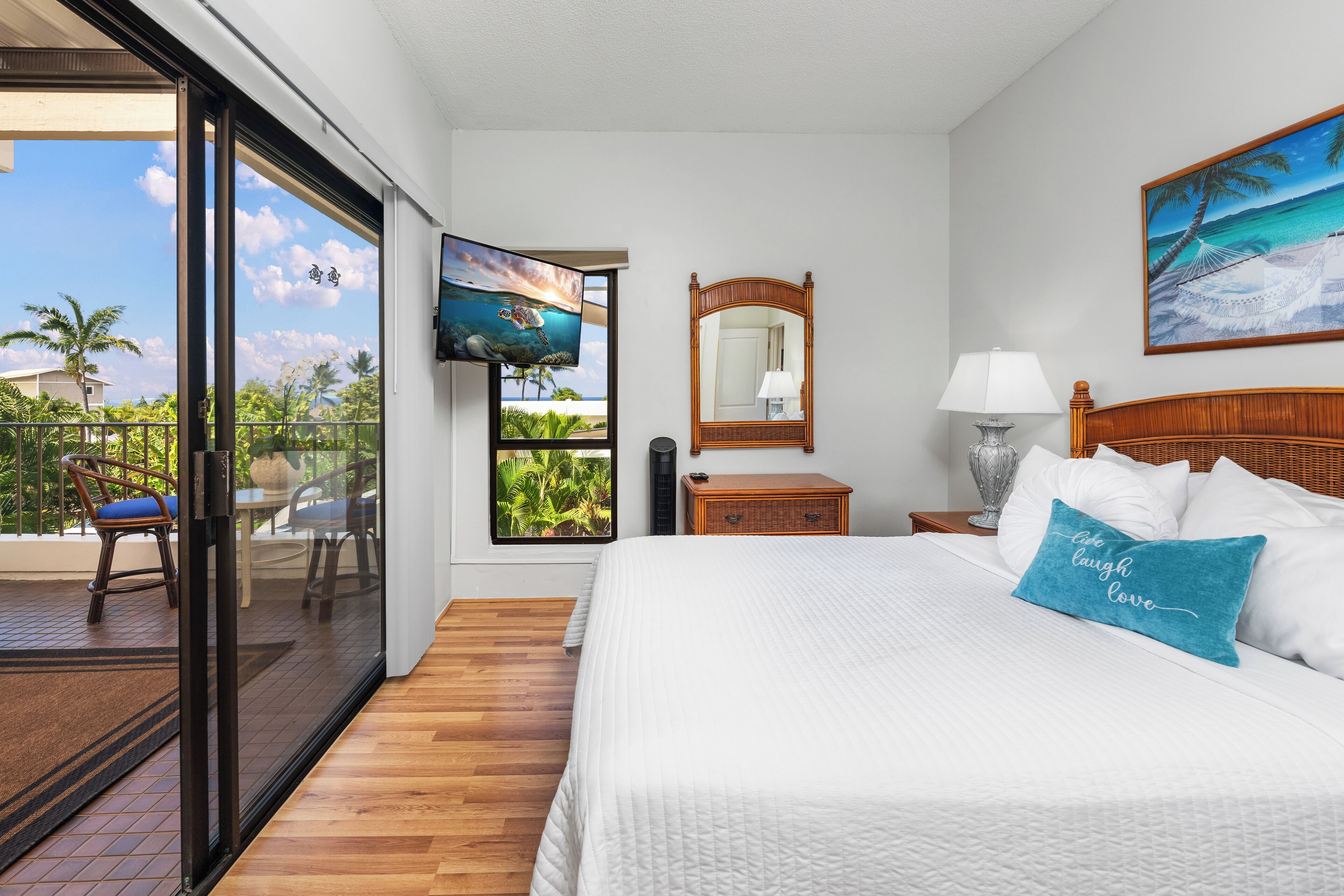 A bedroom with a large bed, a television, a mirror, and a view of the outdoors.