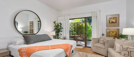 A bedroom with a bed, a round mirror, a ceiling fan, a sofa, and a view of a balcony with plants.