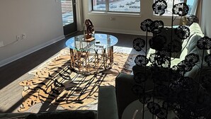 A spacious living room with a large window, a ceiling fan, and a flat-screen TV mounted on the wall. - Charming 1-bedroom apartment with views (Dallas)