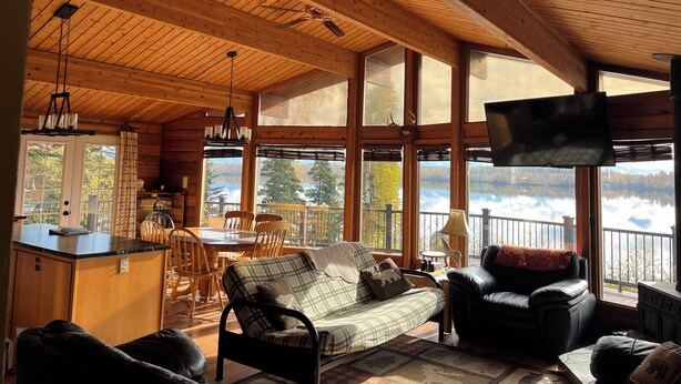 A cabin interior with a dining area, a sofa, a leather chair, and a TV mounted on the wall.