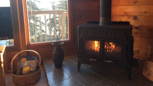 A cozy room with a wood-burning stove, a window with a view of trees, and a basket with books.