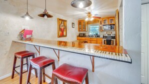 A kitchen with a central island, wooden bar stools, pendant lighting, and a microwave. - 1 Mi to Red Rock Canyon: Old Downtown Loft (Colorado Springs)