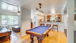 A pool table in a room with hardwood floors, a ceiling fan, and a kitchen area with wooden cabinets and a microwave. - 1 Mi to Red Rock Canyon: Old Downtown Loft (Colorado Springs)