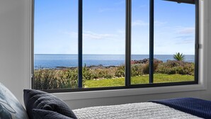 Een slaapkamer met een groot raam met uitzicht op een kustlandschap.