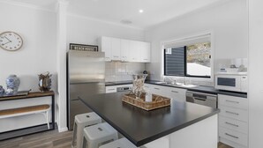 Een moderne keuken met witte kasten, een roestvrijstalen koelkast, een groot raam en een klok aan de muur.