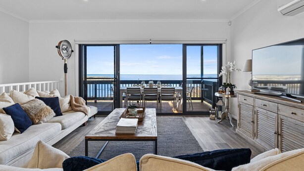 Een ruime woonkamer met een grote schuifpui die uitkomt op een balkon met uitzicht op zee.