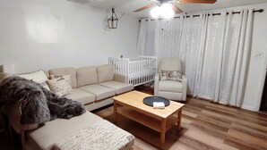 Un salon comprenant un canapé, un fauteuil, une petite table, un berceau et un ventilateur de plafond.