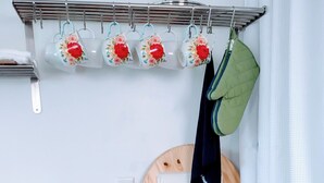 Une cuisine avec un plan de travail en bois, une cuisinière, un porte-ustensiles suspendu orné de tasses à motifs floraux et un pot vert.