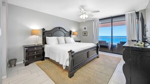 Une chambre à coucher avec un lit, des tables de chevet, une commode, un ventilateur de plafond et une vue sur l’océan.