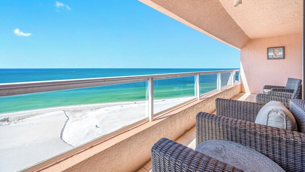 Un balcon doté de meubles en osier, offrant une vue sur une plage et l’océan.