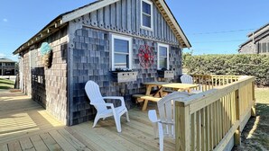 Une maison en bois avec une terrasse, des chaises en plastique blanc et une table en bois.