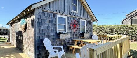 A wooden house with a deck, white plastic chairs, and a wooden table.