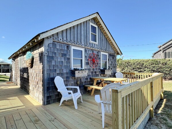 A wooden house with a deck, white plastic chairs, and a wooden table.