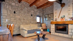 Ein rustikaler Raum mit Steinwand, Kamin, Holztisch, weißem Sofa und sichtbarem Holzbalken an der Decke.