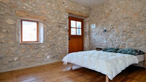 Ein Schlafzimmer mit Steinwand, Holztür, Fenster und einem Bett mit weißer Bettdecke.