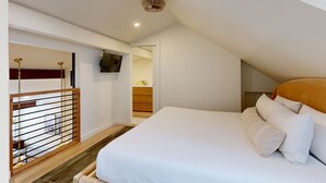 A bedroom with a large bed, a wooden staircase, a TV mounted on the wall, and a ceiling light. - JHRL - Hollyhock 2023 (Wilson)
