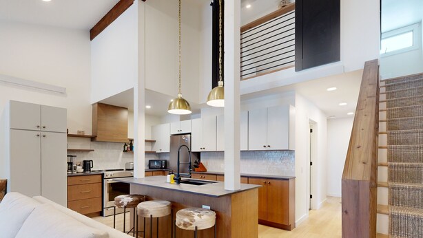 A modern kitchen with a central island, bar stools, and pendant lighting. - JHRL - Hollyhock 2023 (Wilson)