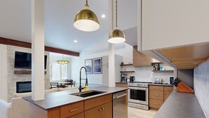 A modern kitchen with a central island, stainless steel appliances, wooden cabinets, and pendant lighting. - JHRL - Hollyhock 2023 (Wilson)