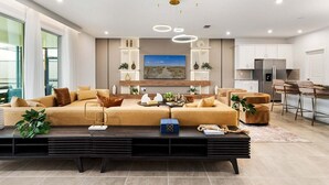 A modern living room with a large sofa, a coffee table, and a dining area with bar stools. - Orlando Oasis: Themed Rooms, Pool & Surf Simulator (Kissimmee)
