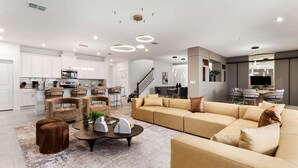 A modern living room with a sectional sofa, a coffee table, and a dining area with chairs. - Orlando Oasis: Themed Rooms, Pool & Surf Simulator (Kissimmee)