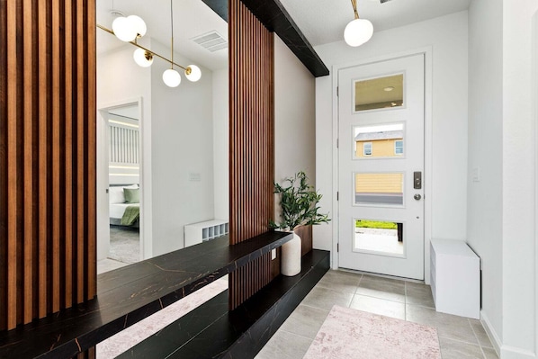 A modern hallway with a black marble bench, a wooden slat wall, a potted plant, and a white door with windows.