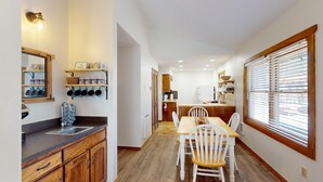 A compact kitchen with wooden cabinets, a built-in oven, and a dining area with a wooden table and chairs. - Ski-in Ski-out  | Large Windows | High Ceilings | Gold Creek 307 (Angel Fire)
