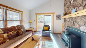 A cozy living room with a sofa, a chair, a fireplace, and a stone wall. - Ski-in Ski-out  | Large Windows | High Ceilings | Gold Creek 307 (Angel Fire)
