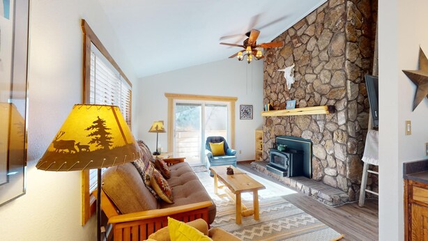 A cozy living room with a stone fireplace, a ceiling fan, and a sofa with a patterned throw. - Ski-in Ski-out  | Large Windows | High Ceilings | Gold Creek 307 (Angel Fire)