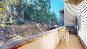 A patio with a concrete barrier, a wooden table, and two bar stools. - Ski-in Ski-out  | Large Windows | High Ceilings | Gold Creek 307 (Angel Fire)