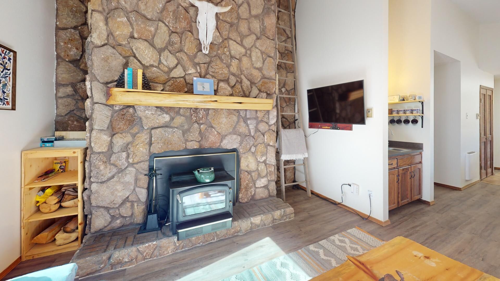 A cozy living area with a stone fireplace, a television mounted on the wall, and a kitchen area with wooden cabinets and a countertop.