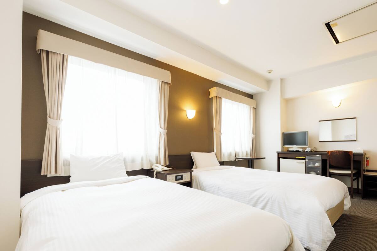 A hotel room with two beds, a desk with a computer, a chair, and a TV.