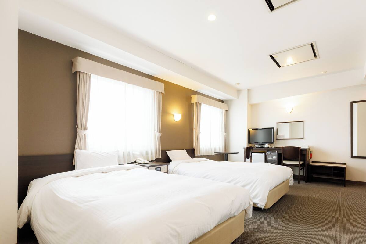 A hotel room with two beds, a desk with a TV, and a small seating area.