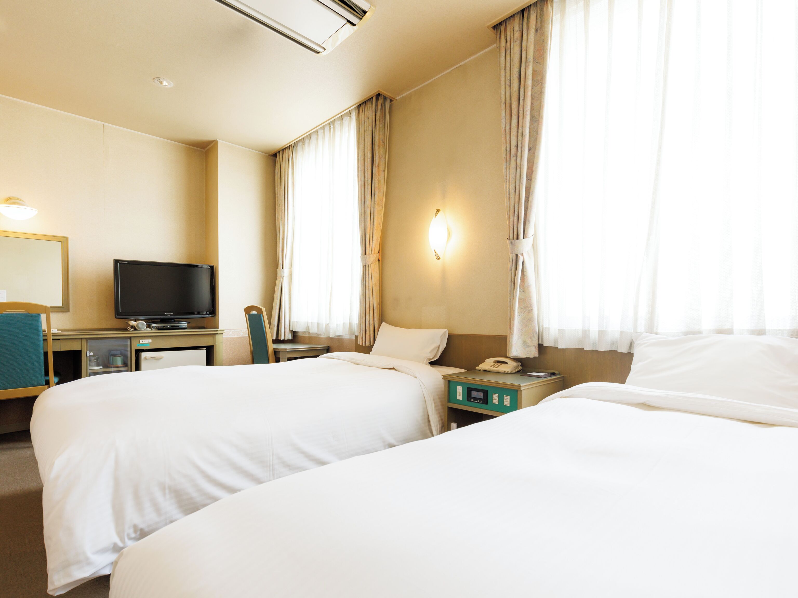 Quarto de hotel com duas camas, televisão, escrivaninha e telefone.