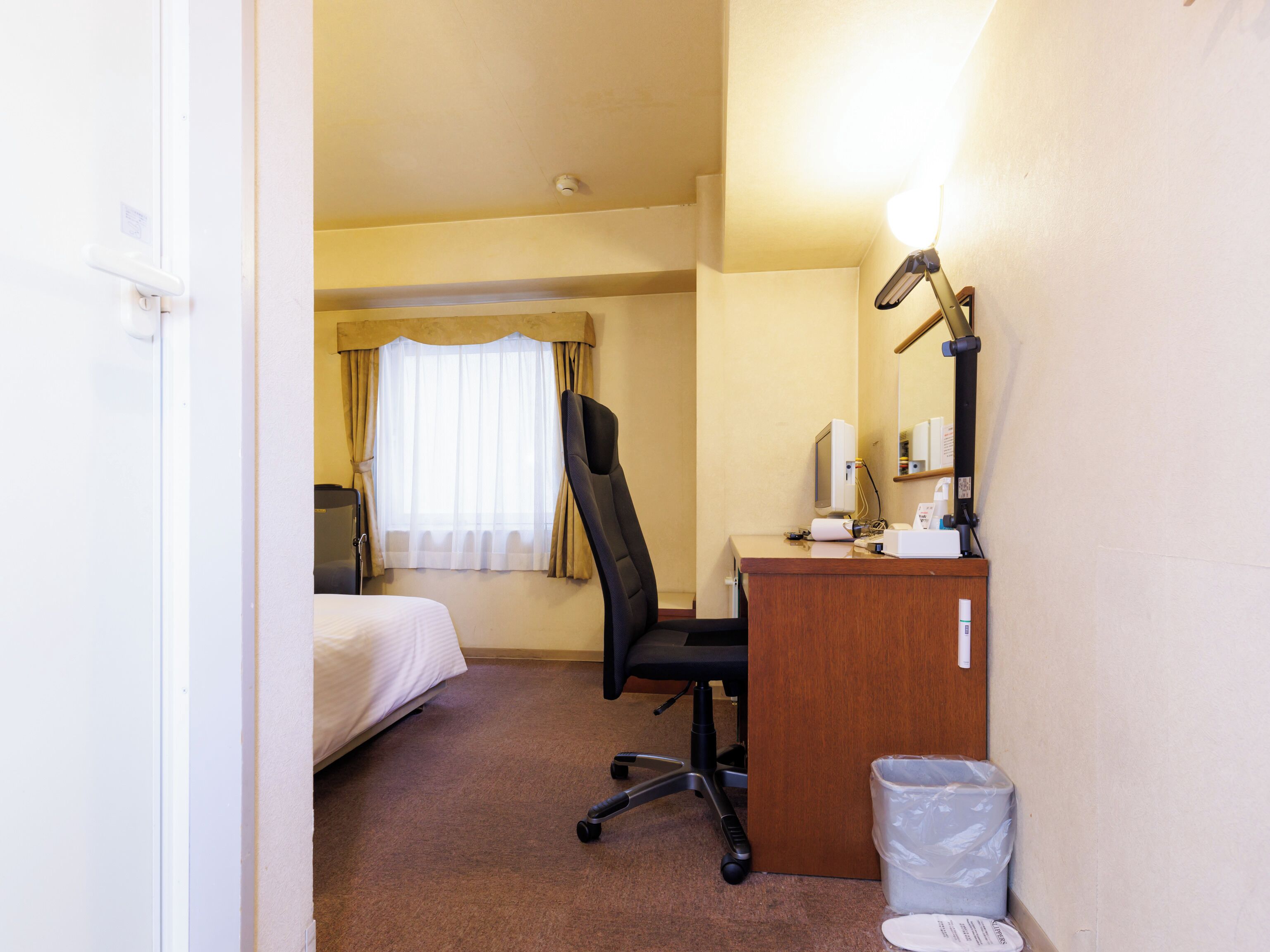 Une chambre d’hôtel avec un lit, un bureau doté d’une lampe, une chaise et une poubelle.