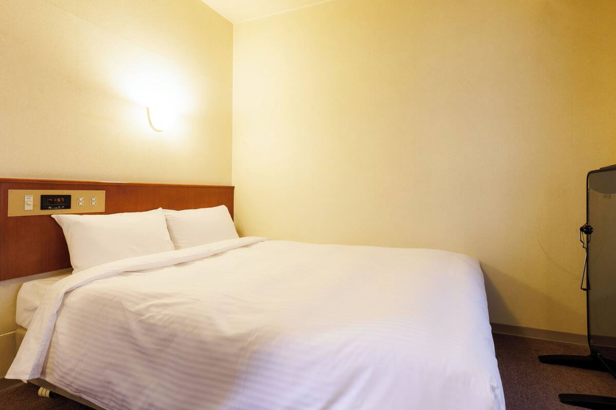 A hotel room with a bed, a control panel, and a mirror.